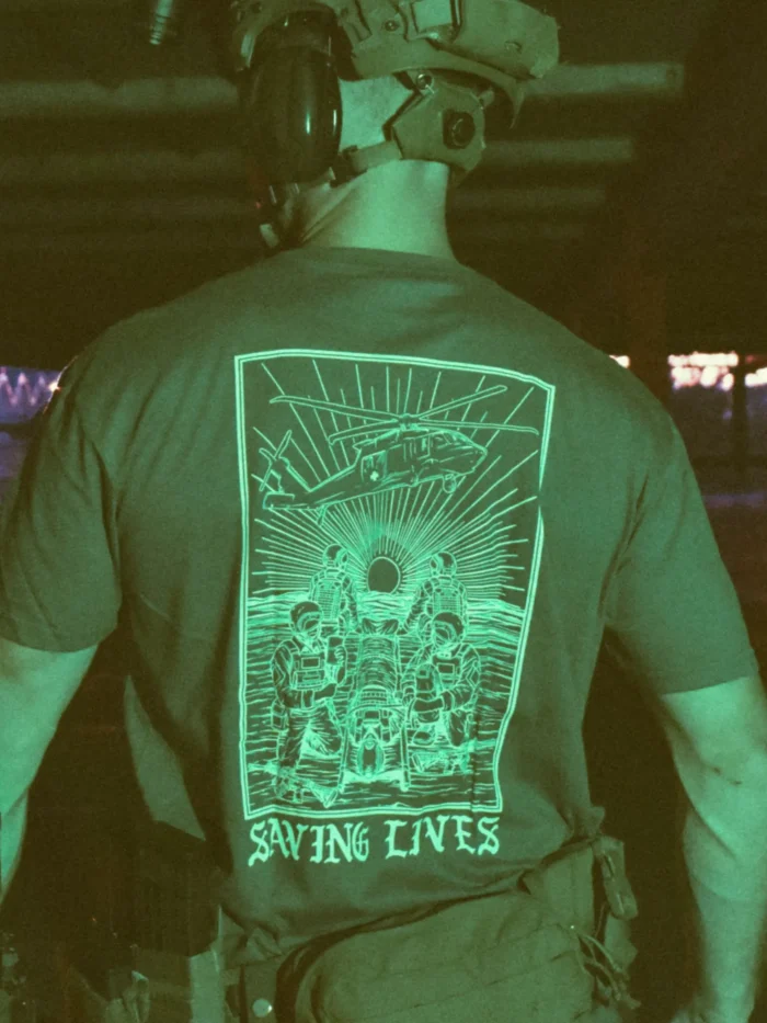 Cotton T-shirt with Saving Lives artwork showing soldiers in action, holding a stretcher during a tense medevac moment with a helicopter descending nearby.