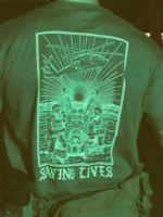 Cotton T-shirt with Saving Lives artwork showing soldiers in action, holding a stretcher during a tense medevac moment with a helicopter descending nearby.