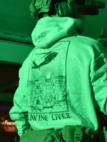 Military-style hoodie featuring the Saving Lives design: a group of soldiers carrying a stretcher while a helicopter prepares to land, symbolizing courage under pressure.