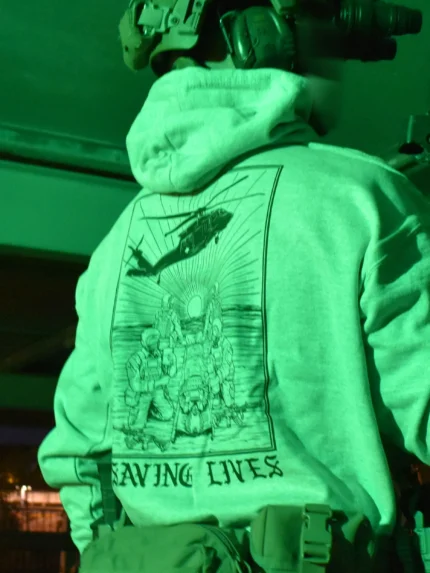 Military-style hoodie featuring the Saving Lives design: a group of soldiers carrying a stretcher while a helicopter prepares to land, symbolizing courage under pressure.