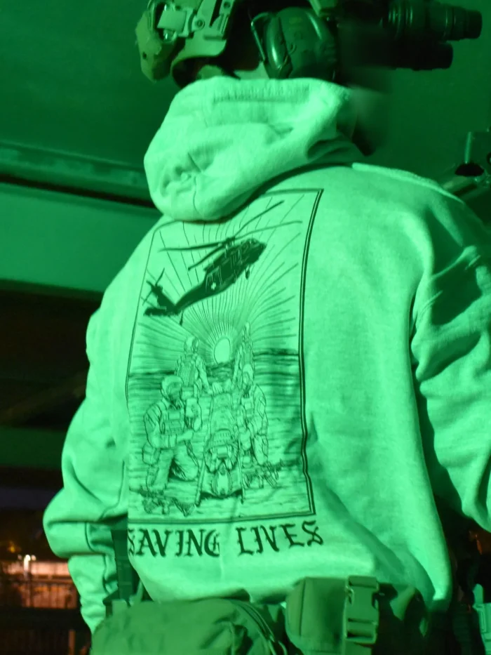 Military-style hoodie featuring the Saving Lives design: a group of soldiers carrying a stretcher while a helicopter prepares to land, symbolizing courage under pressure.