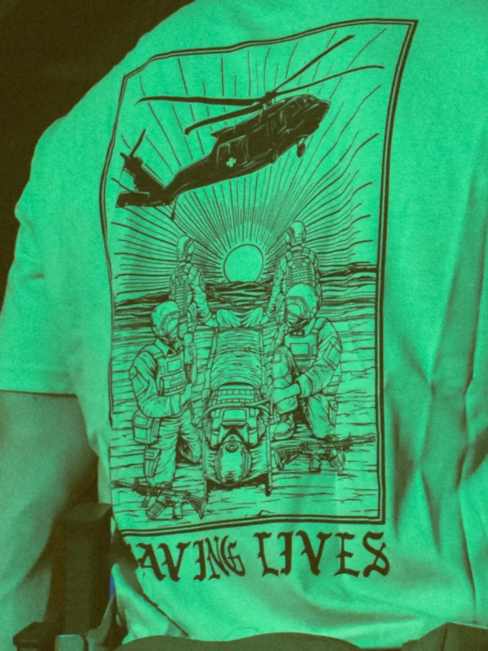 Cotton T-shirt with Saving Lives artwork showing soldiers in action, holding a stretcher during a tense medevac moment with a helicopter descending nearby.