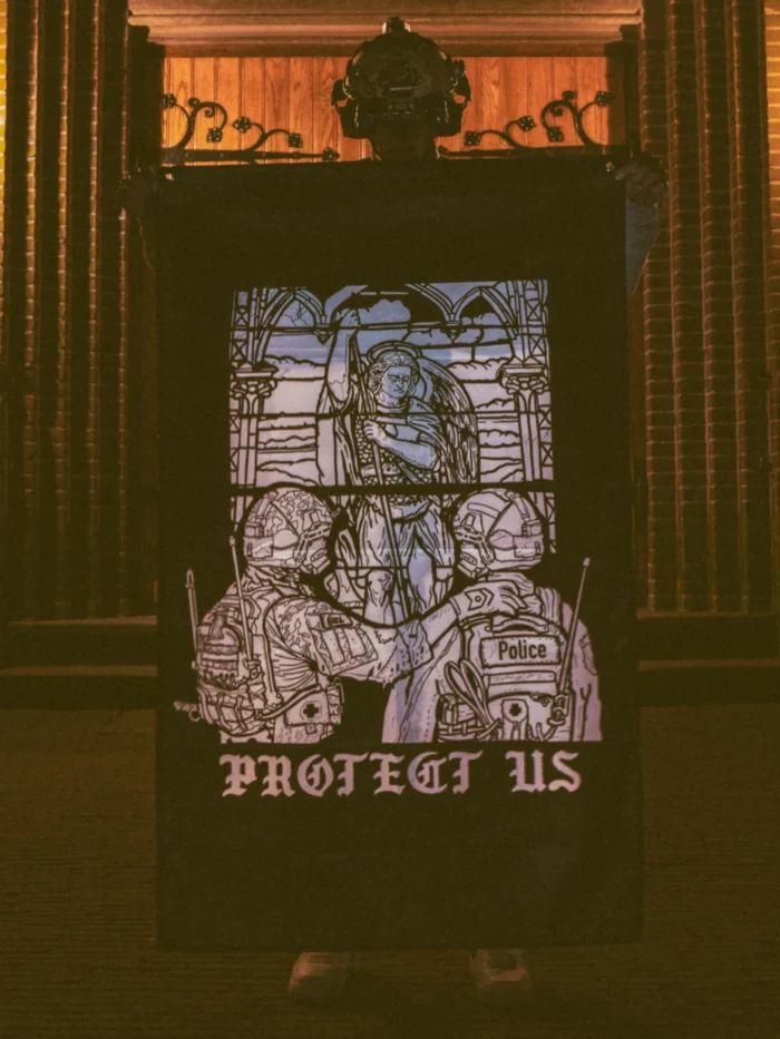 the trace apparel collection featuring a military and a police guy standing in front of a tinted window that displays saint michael the protector